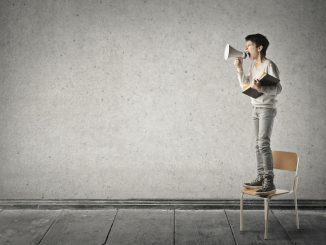 Little boy is standing on a chair and shouting with a megaphone